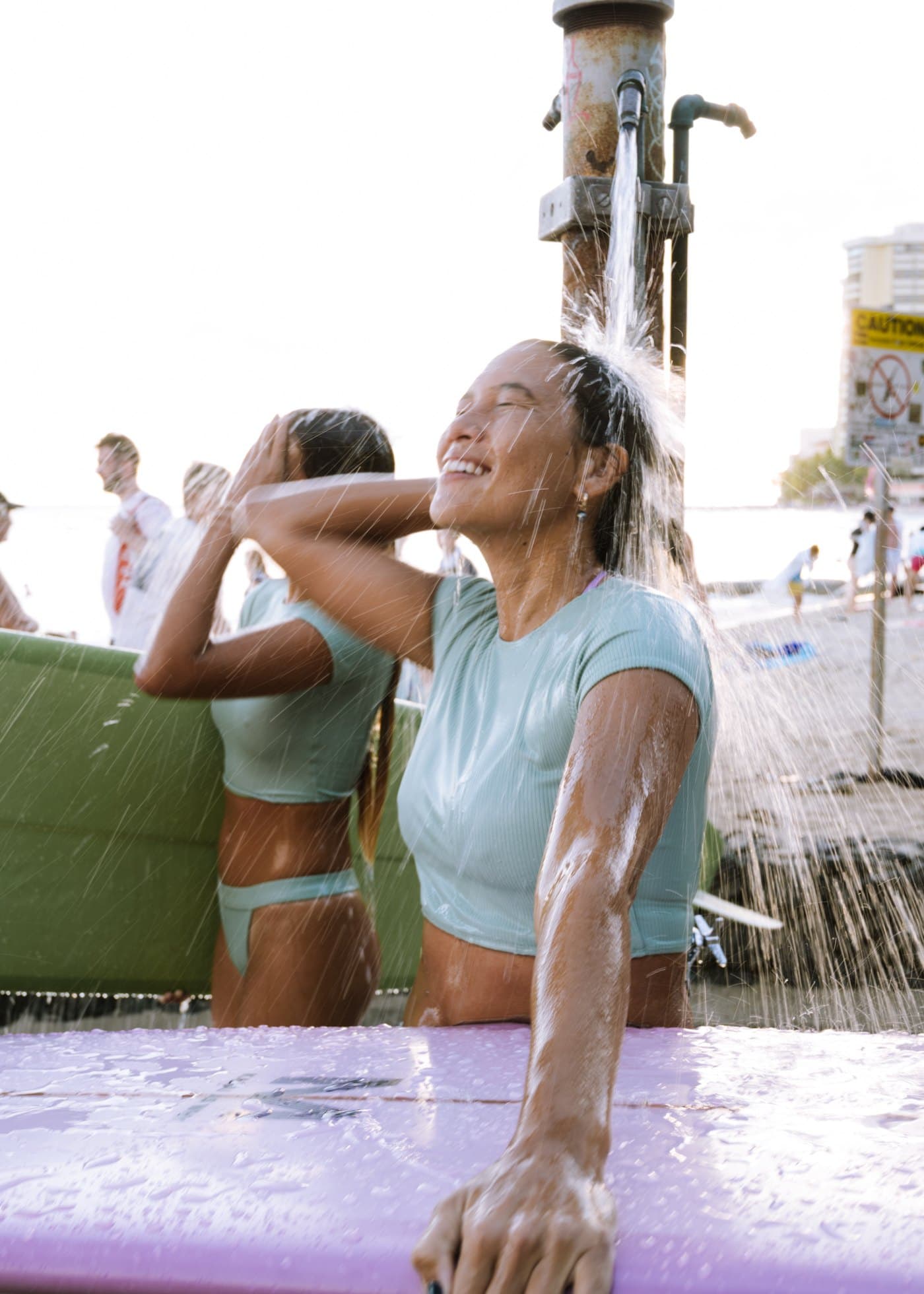 Model rinsing off at the Waikīkī beach shower, mint crop top