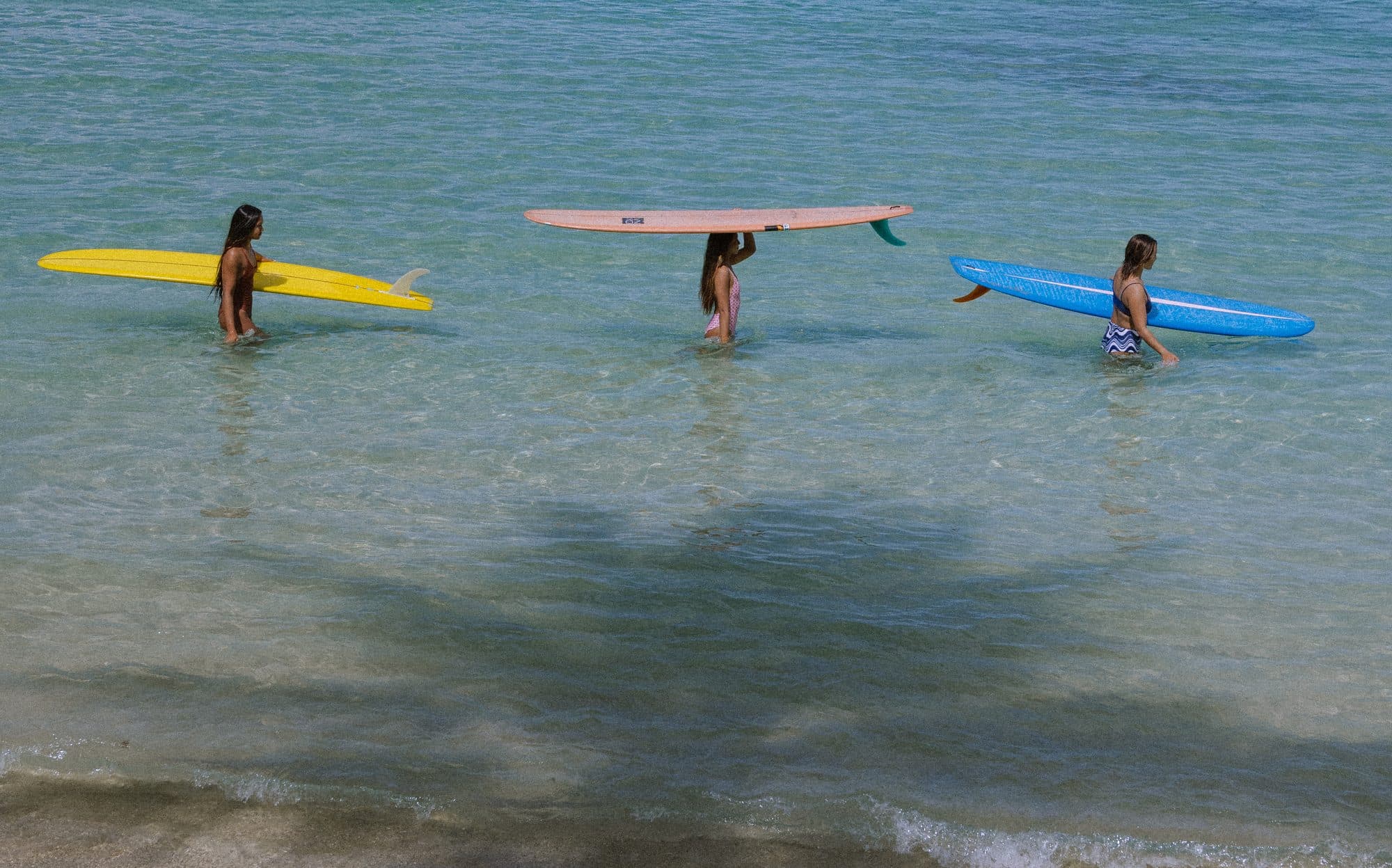 Three surfers on longboards seen from above in clear water