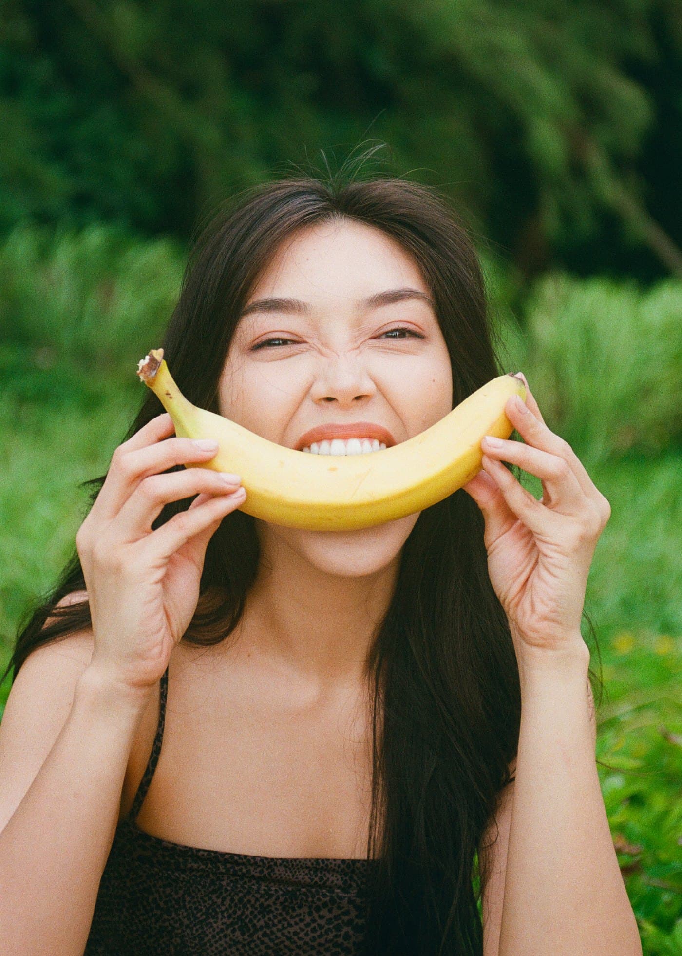 Model smiling with a banana in front of green foliage